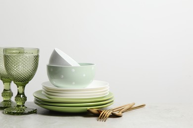 Beautiful ceramic dishware, glasses and cutlery on light grey table, space for text