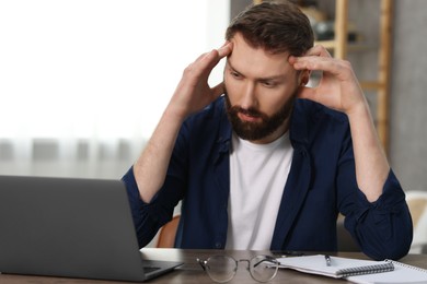 Overwhelmed man sitting with laptop at table indoors