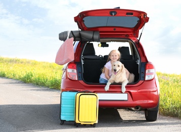 Photo of Cute little girl and her dog in open car trunk outdoors. Space for text