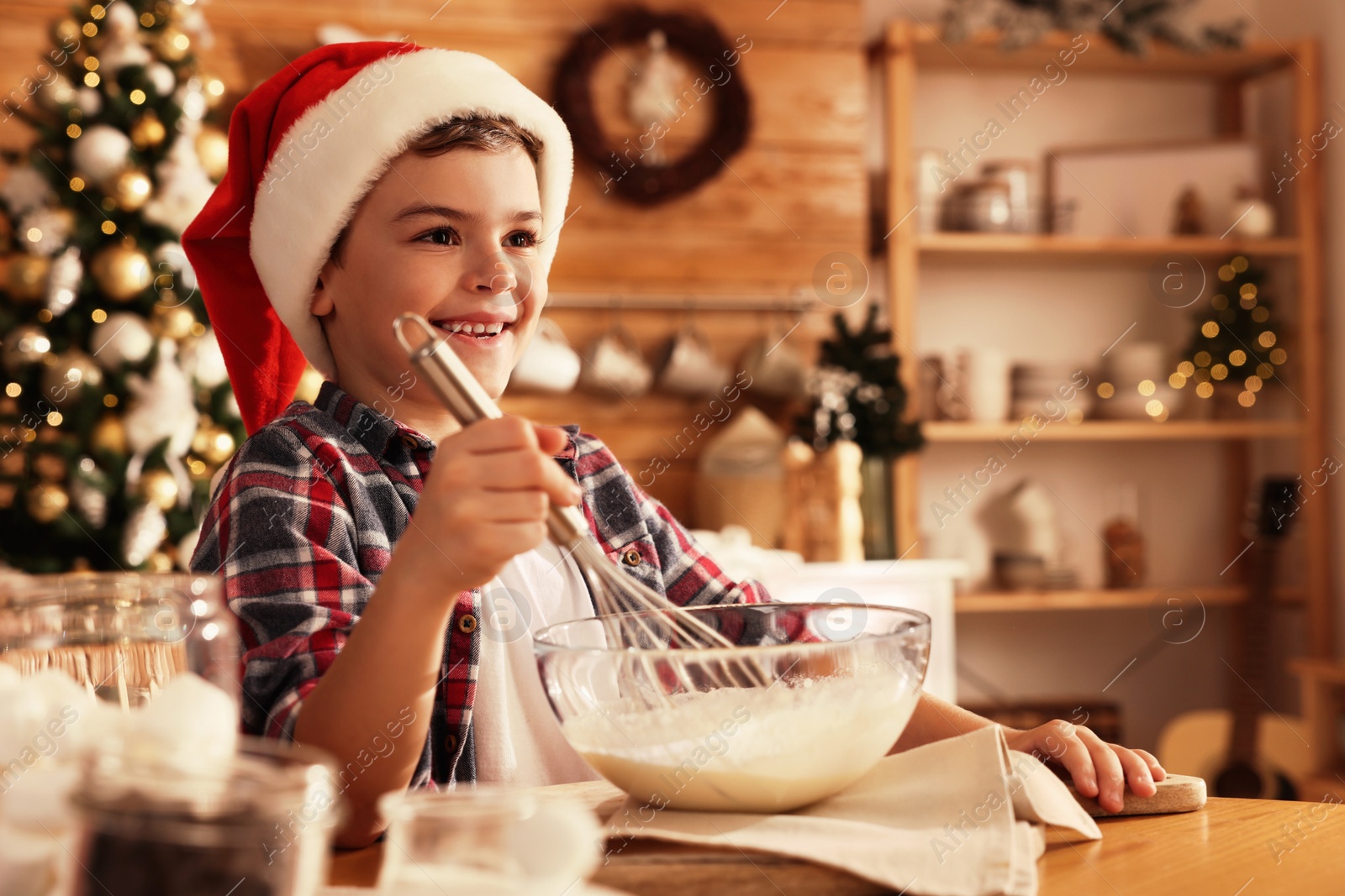 Photo of Cute little boy in Santa hat making dough for Christmas cookies at home