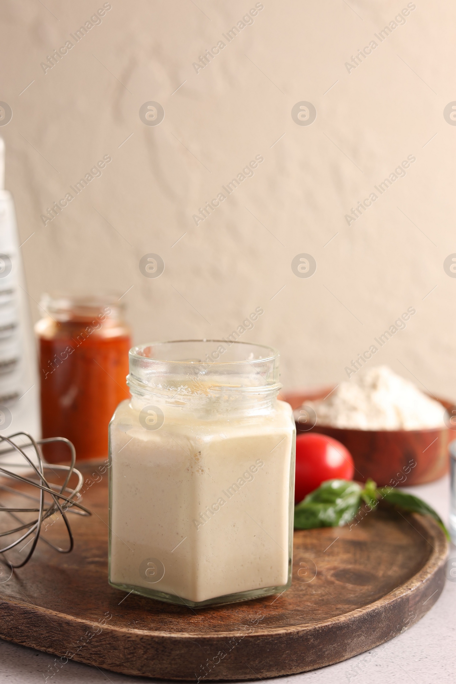 Photo of Pizza dough starter in glass jar and products on gray table