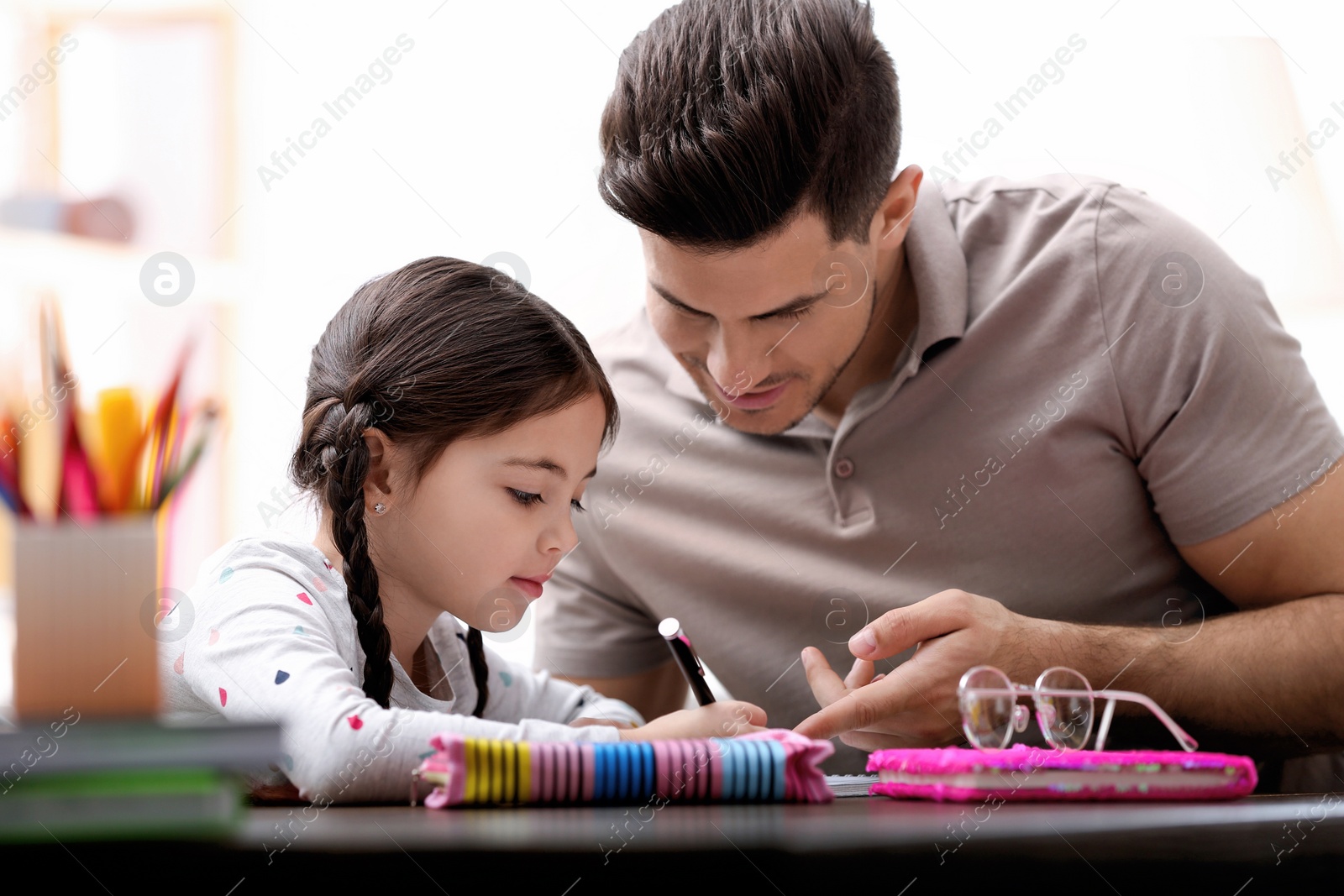 Photo of Man helping his daughter with homework at table indoors