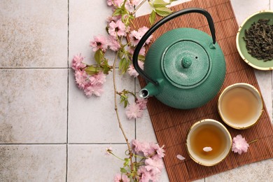 Photo of Traditional ceremony. Cup of brewed tea, teapot, dried leaves and sakura flowers on tiled table, flat lay with space for text