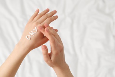 Photo of Young woman with word Dry made of cream on her hand on bed, closeup