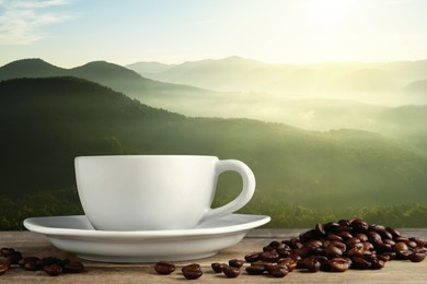 Cup of aromatic hot coffee on wooden table and beautiful view of mountain landscape