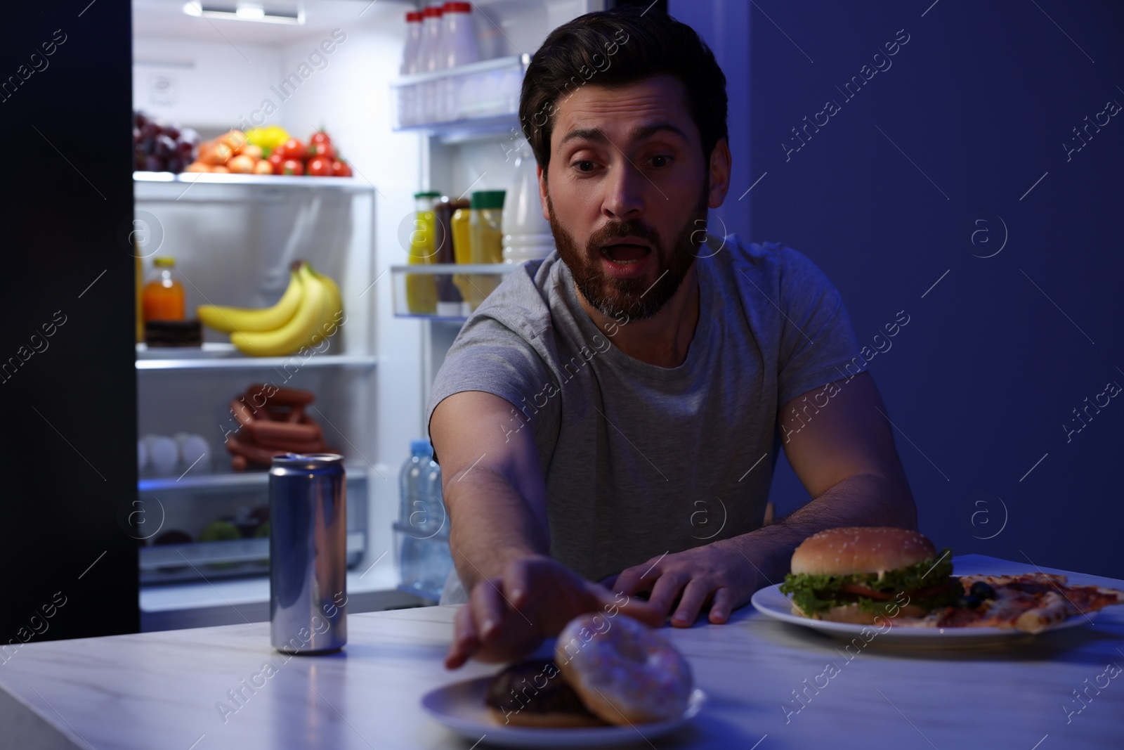 Photo of Man taking donut in kitchen at night. Bad habit