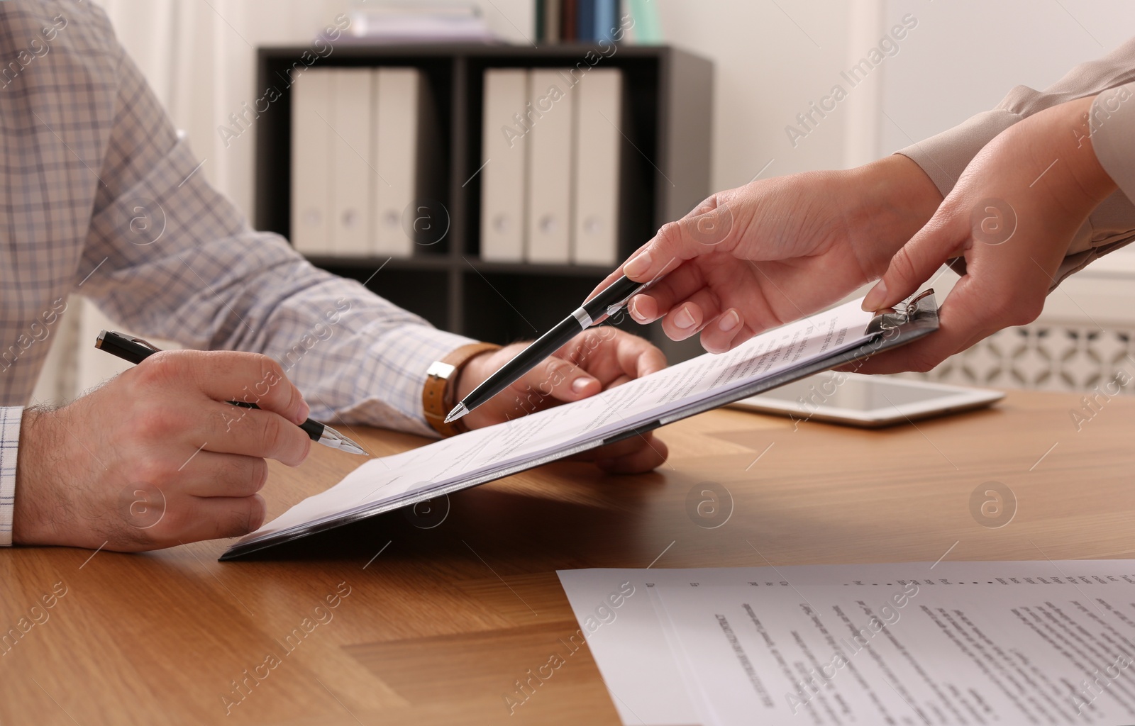 Photo of Businesspeople signing contract at wooden table indoors, closeup of hands