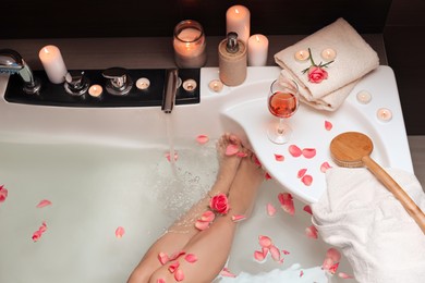 Woman taking bath with rose petals, above view. Romantic atmosphere