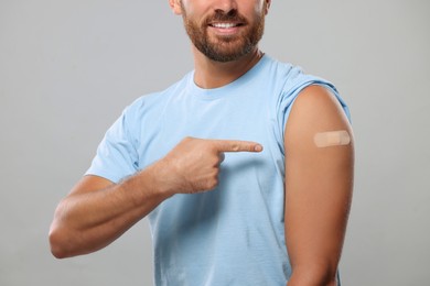 Man pointing at sticking plaster after vaccination on his arm against light grey background, closeup