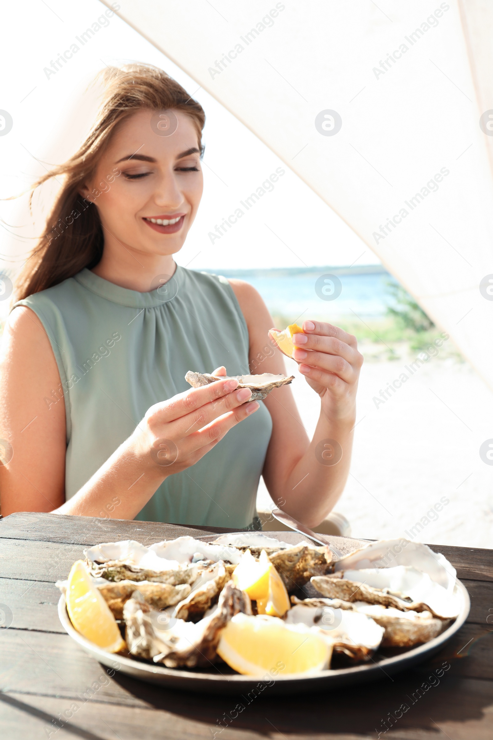 Photo of Woman eating fresh oyster at table, outdoors