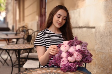 Beautiful woman with bouquet of spring flowers in outdoor cafe