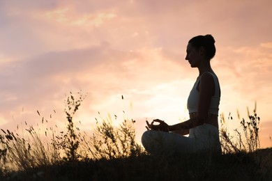 Photo of Mature woman meditating outdoors at sunset. Space for text