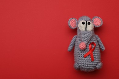 Cute knitted toy mouse with ribbon on red background, top view and space for text. AIDS disease awareness