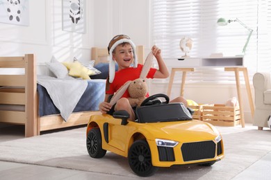 Photo of Cute little boy playing with stuffed bunny and big toy car at home