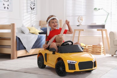 Cute little boy playing with stuffed bunny and big toy car at home