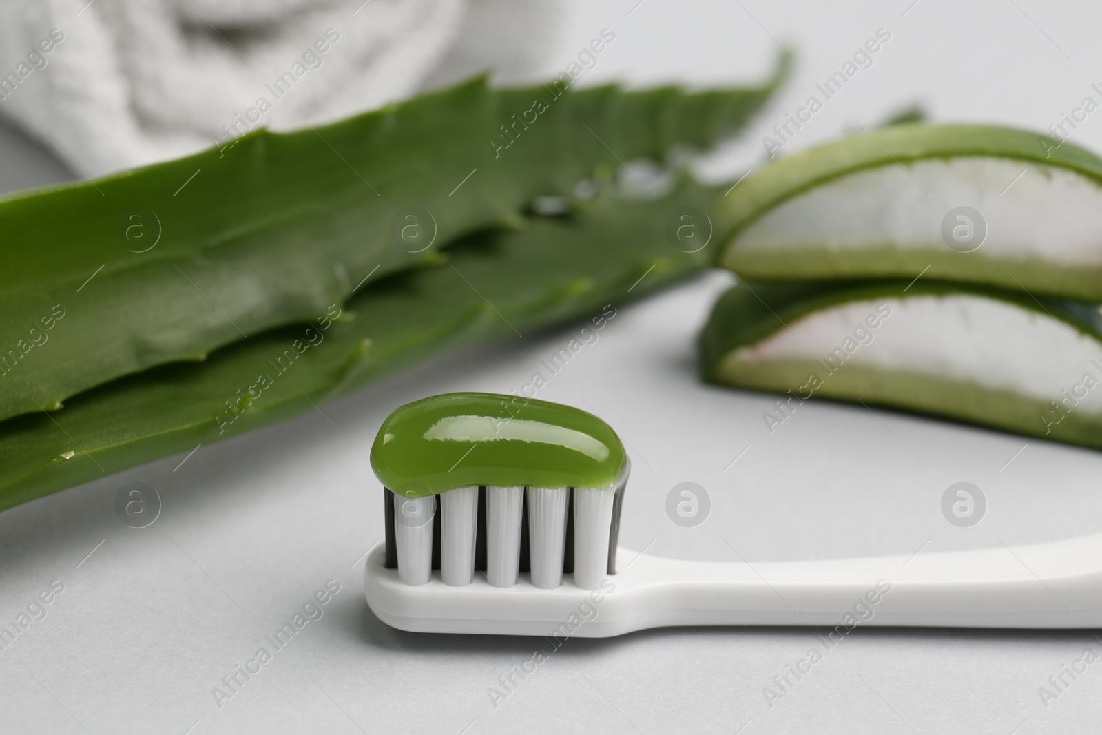 Photo of Toothbrush with toothpaste and fresh aloe on light grey background, closeup