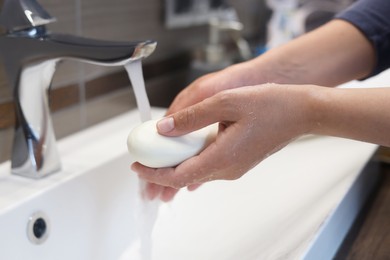 Photo of Woman with soap bar washing hands in bathroom, closeup