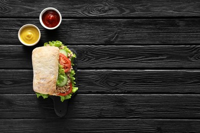 Food photography. Delicious sandwich with tuna, vegetables and sauces on black wooden table, flat lay with space for text