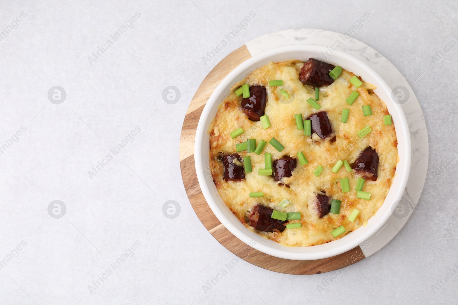 Photo of Tasty sausage casserole with green onions in baking dish on white table, top view. Space for text