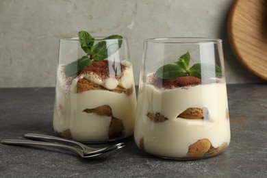 Photo of Delicious tiramisu with mint in glasses on grey table