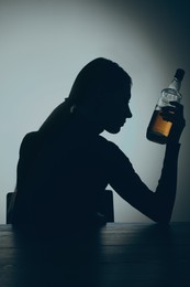 Photo of Alcohol addiction. Silhouette of woman with bottle of whiskey at wooden table, backlit