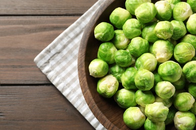 Photo of Bowl of fresh Brussels sprouts and napkin on wooden background, top view with space for text