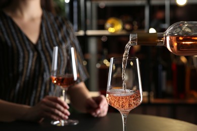 Photo of Pouring rose wine from bottle into glass indoors, closeup. Space for text