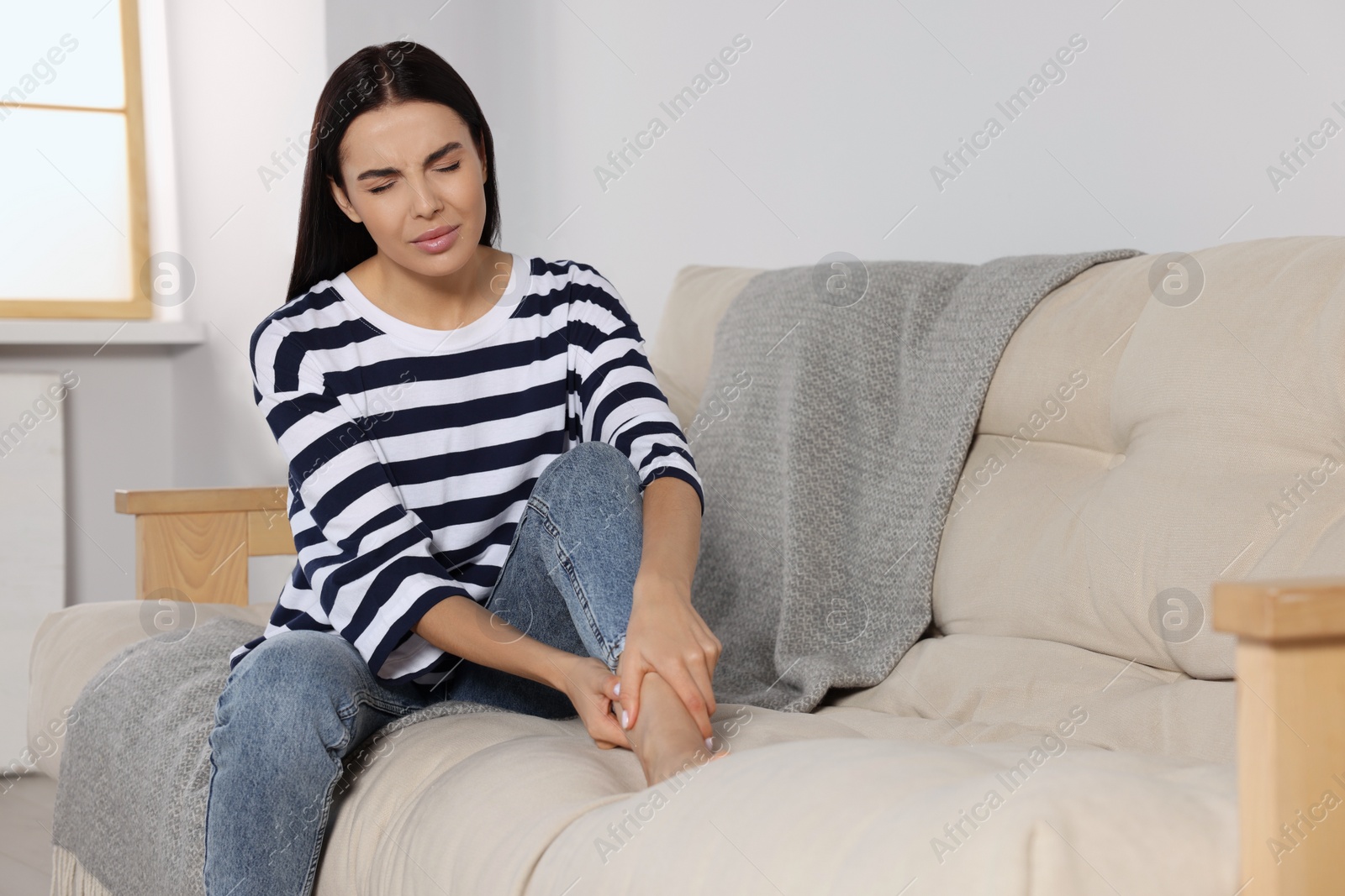 Photo of Woman suffering from leg pain on sofa at home, space for text