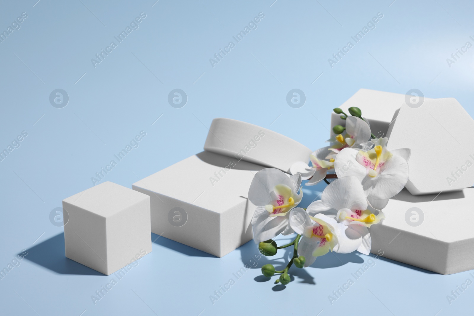 Photo of Scene for product presentation. Podiums of different geometric shapes and orchid flowers on light blue background