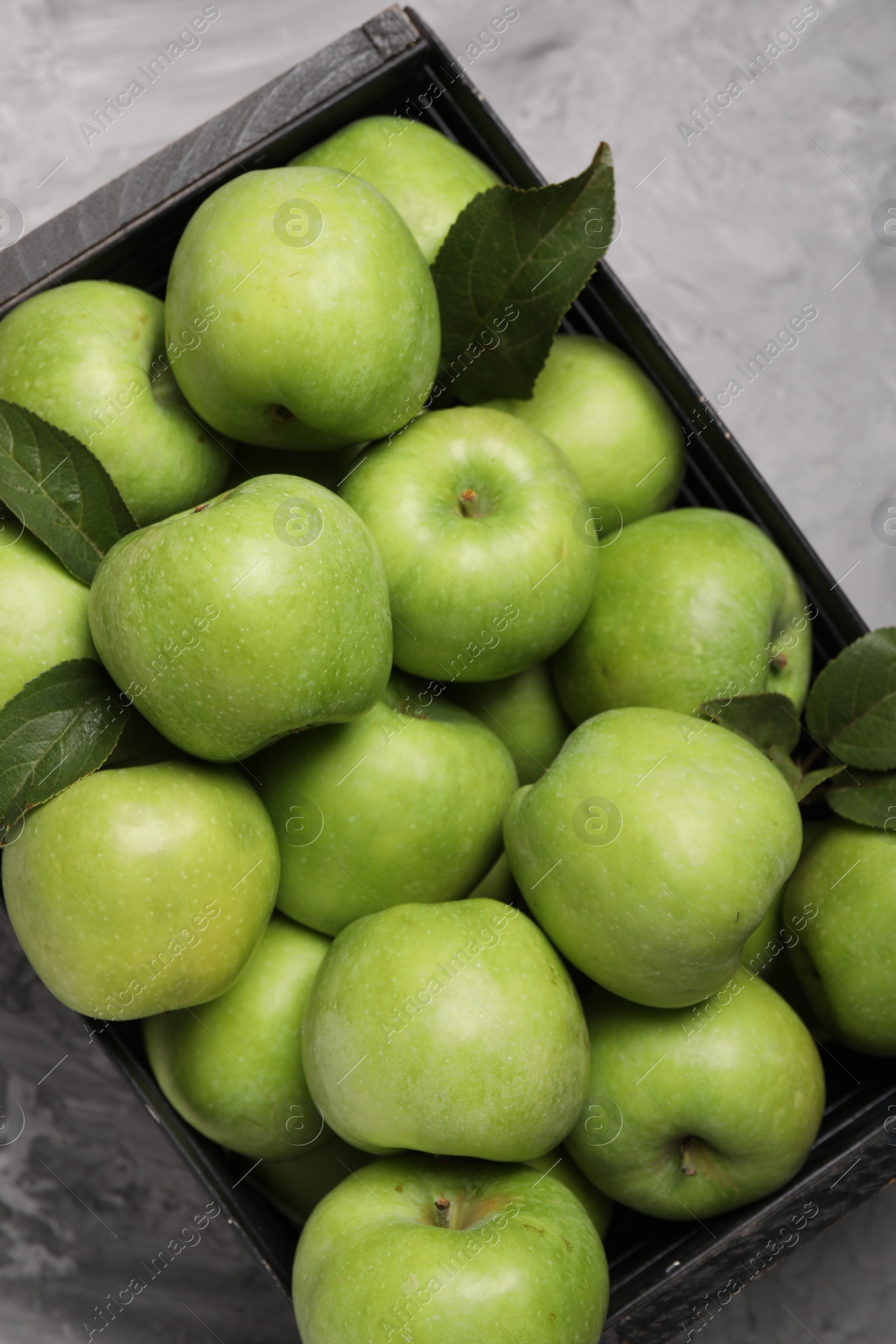 Photo of Fresh green apples in crate on grey textured table, top view