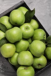 Fresh green apples in crate on grey textured table, top view