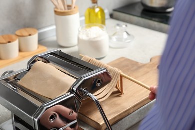 Woman making soba with pasta machine at table in kitchen, closeup