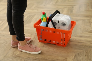 Photo of Woman and shopping basket with household goods on wooden floor, closeup