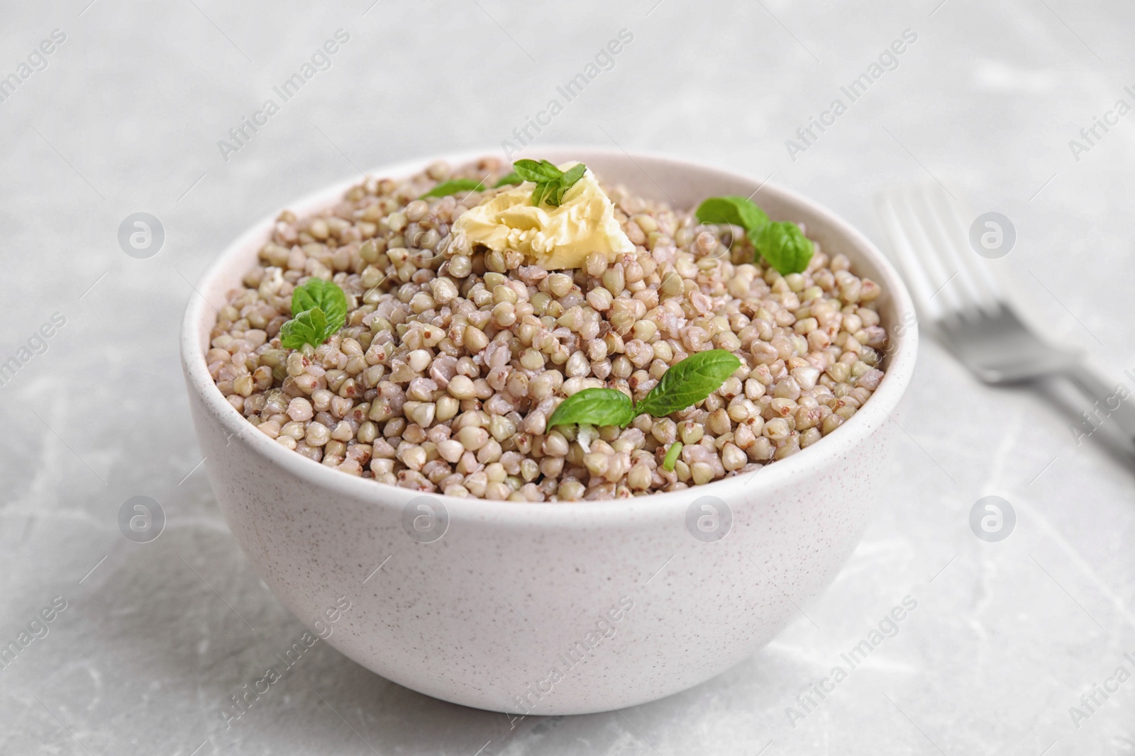 Photo of Tasty buckwheat porridge with butter on grey marble table