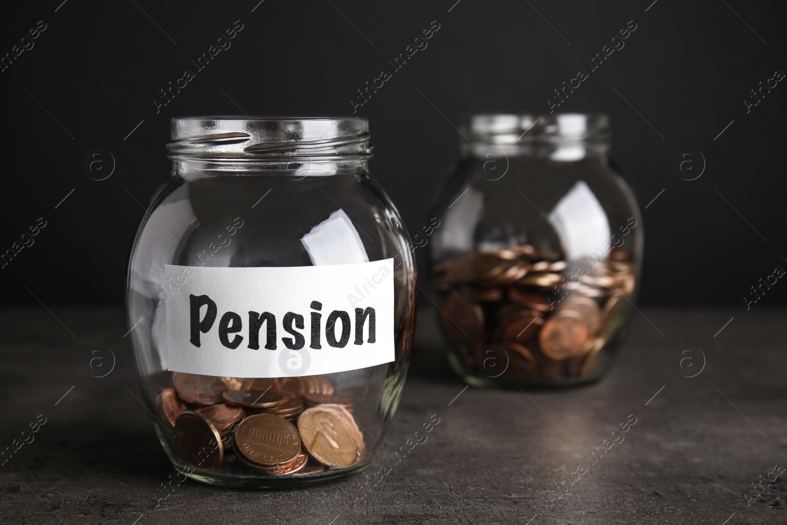 Photo of Glass jars with coins and label PENSION on dark table