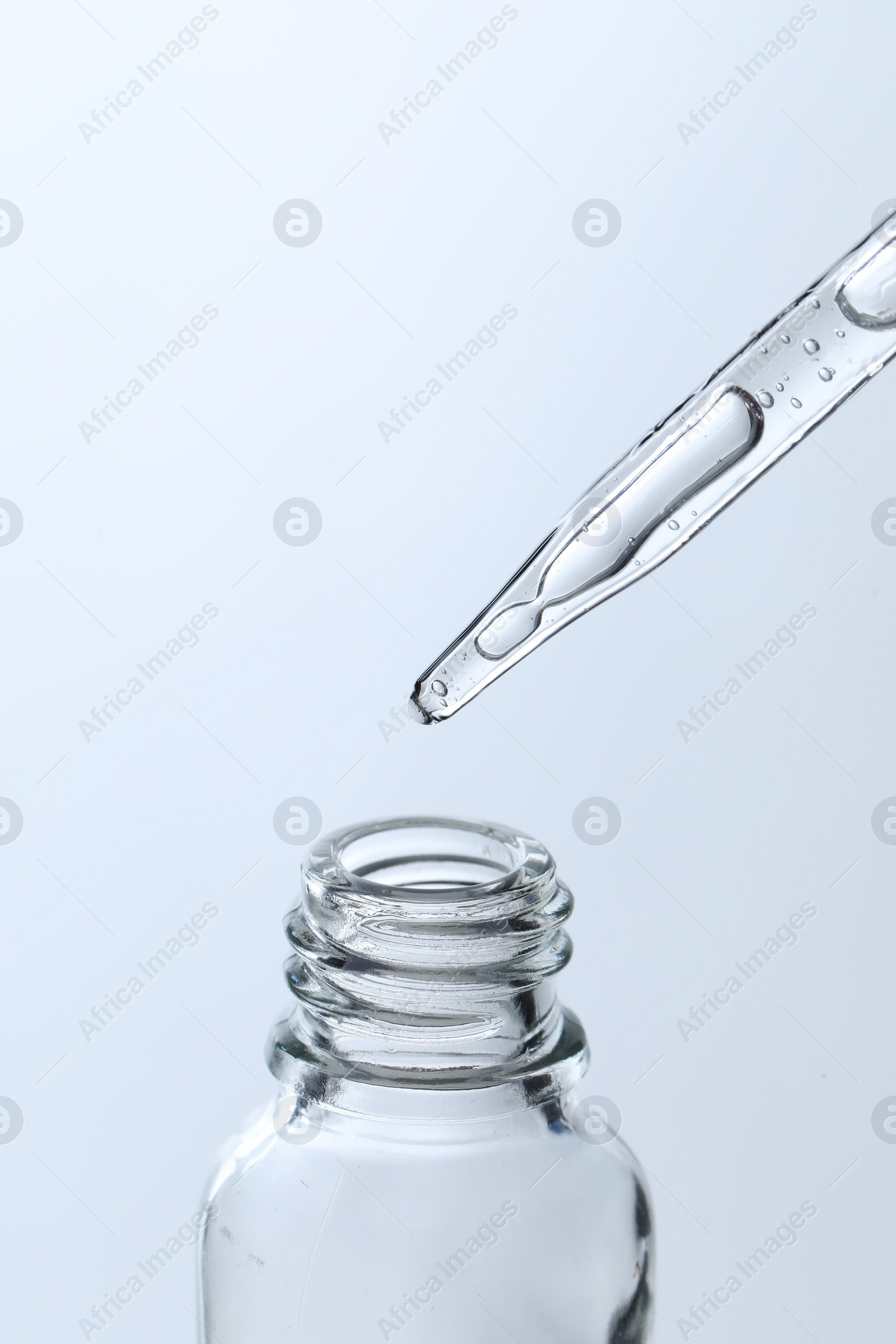 Photo of Dripping liquid from pipette into glass bottle on light blue background, closeup