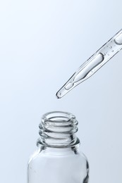 Dripping liquid from pipette into glass bottle on light blue background, closeup