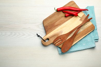 Photo of Cutting board with peppers and cooking utensils on white wooden table, top view. Space for text