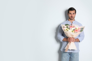 Photo of Young handsome man with beautiful flower bouquet on light background, space for text