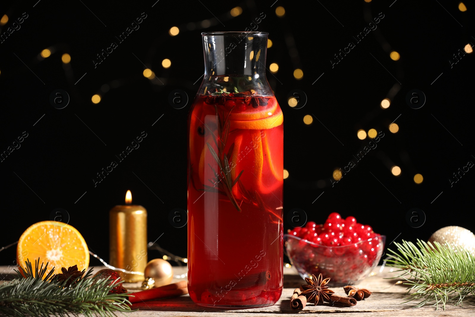 Photo of Glass bottle of aromatic punch drink, ingredients and Christmas decor on wooden table