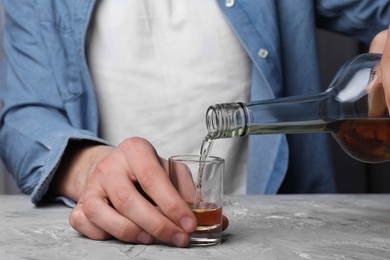 Alcohol addiction. Man pouring whiskey from bottle into glass at grey textured table, closeup