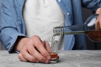 Photo of Alcohol addiction. Man pouring whiskey from bottle into glass at grey textured table, closeup