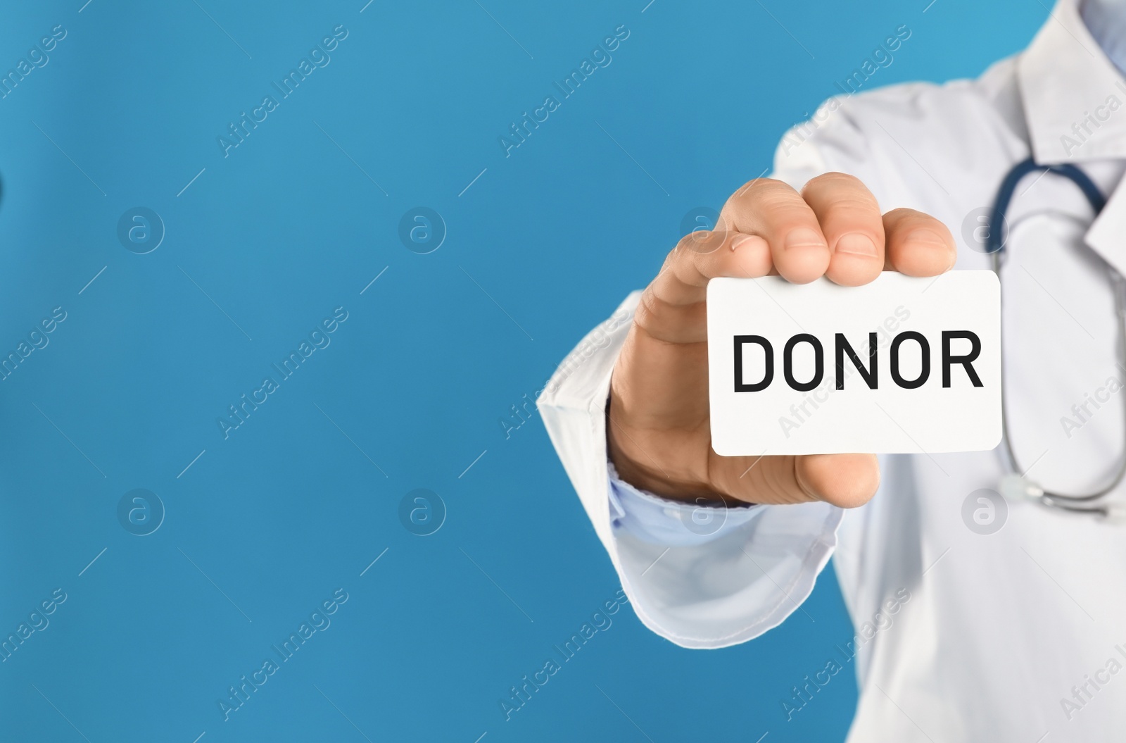 Image of Doctor holding card with word DONOR on light blue background, closeup. Space for text