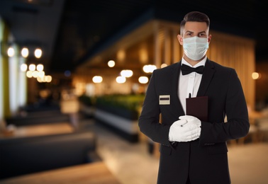 Image of Waiter in medical face mask holding notebook at outdoor cafe