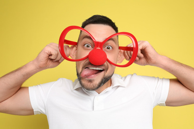 Photo of Funny man with clown nose and large glasses on yellow background. April fool's day