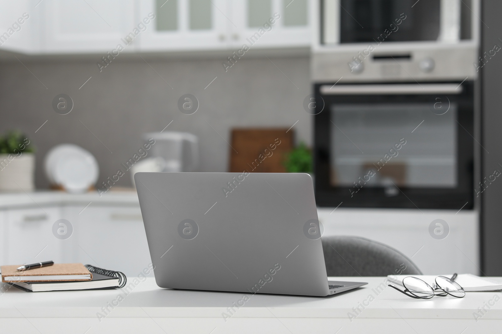 Photo of Home office. Laptop, glasses and stationery on white desk in kitchen