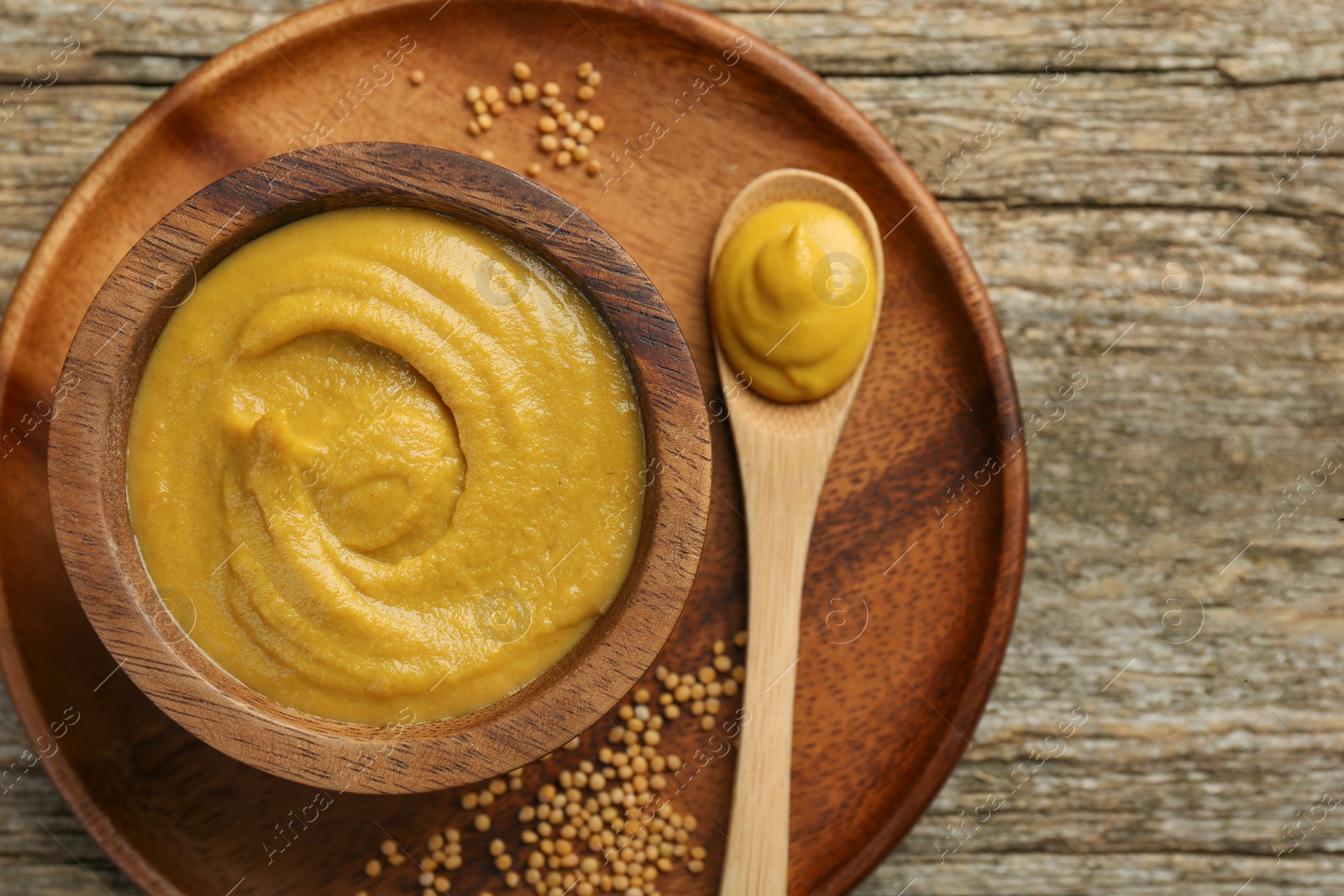 Photo of Spoon and bowl of tasty mustard sauce with dry seeds on wooden table, top view