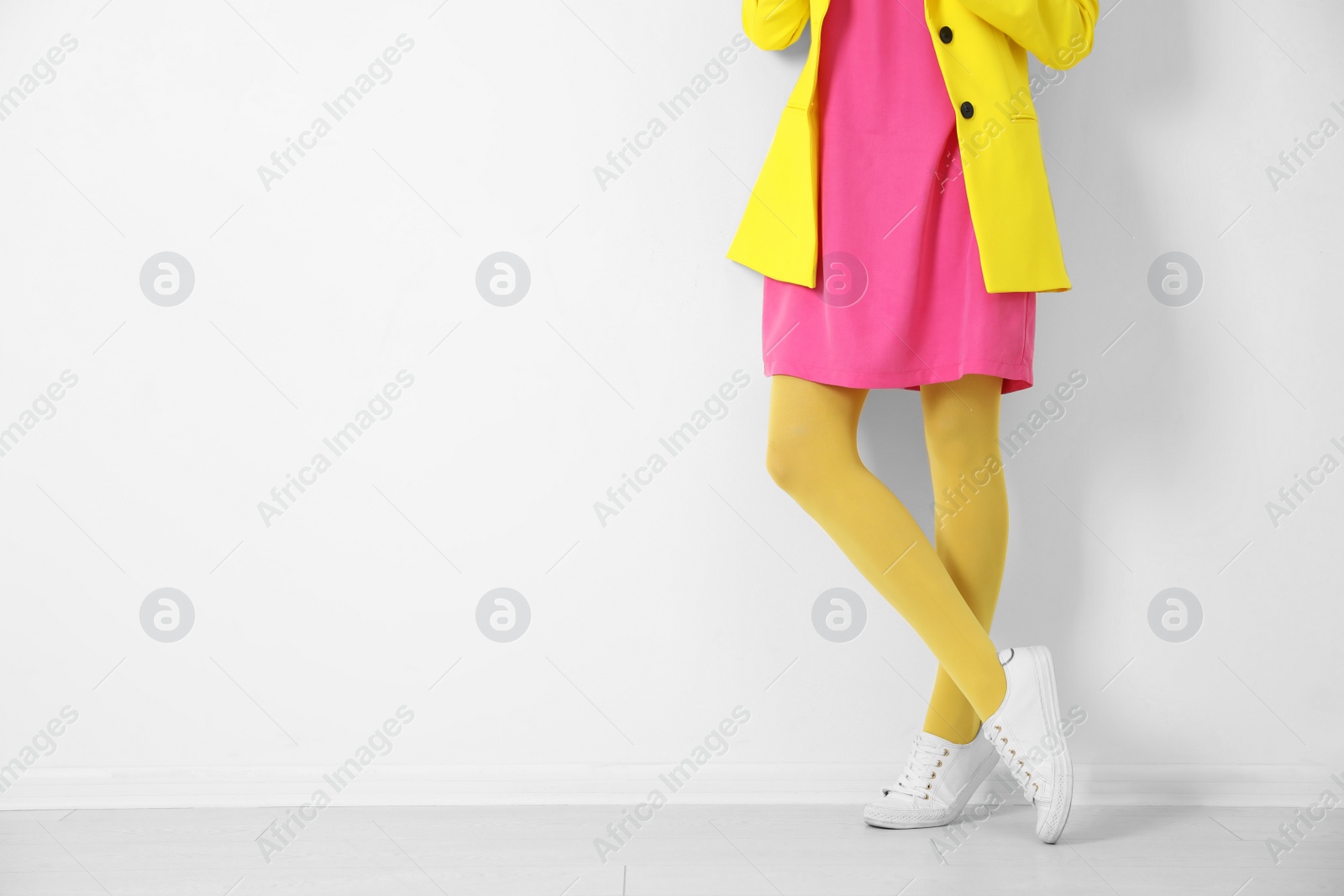 Photo of Woman wearing yellow tights near white wall, closeup. Space for text