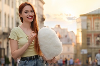 Photo of Smiling woman with cotton candy on city street. Space for text