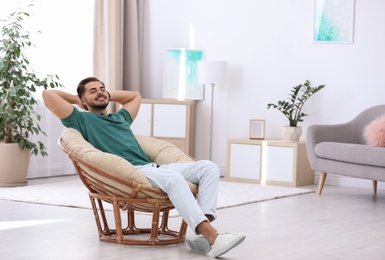 Handsome young man sitting in armchair at home. Space for text